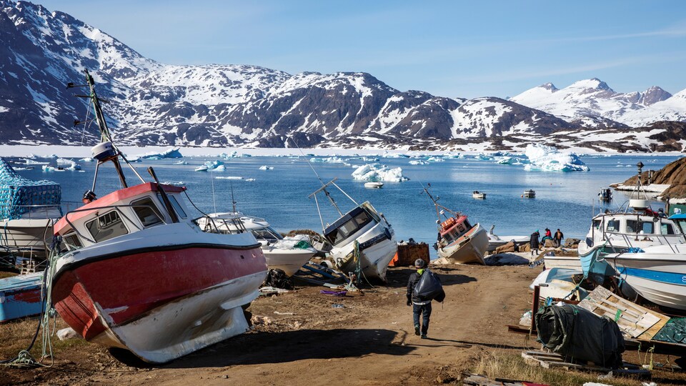 Un paysage du Groenland où l'on retrouve des bateaux, une étendue d'eau et des montagnes.