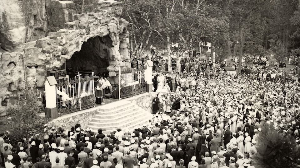 Des dizaines de personnes sont rassemblées devant l'entrée d'une grotte où des religieux tiennent une cérémonie.