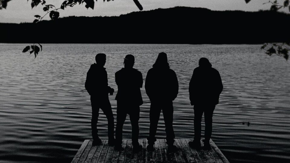 Quatre musiciens de dos près d'un lac.