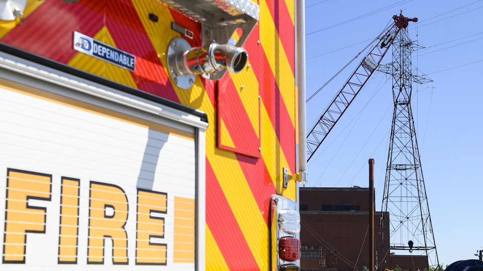 Un camion de pompier devant une grue qui touche des fils électriques suspendus à un pylône.