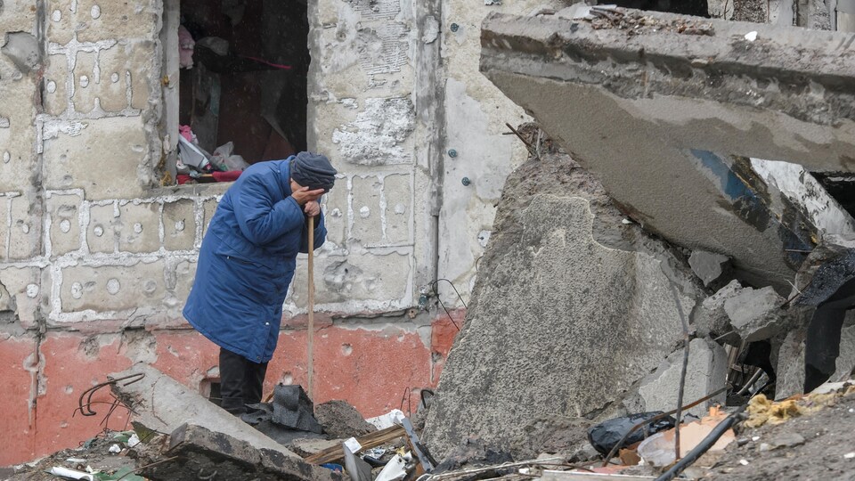 A woman is crying near the rubble of a house.