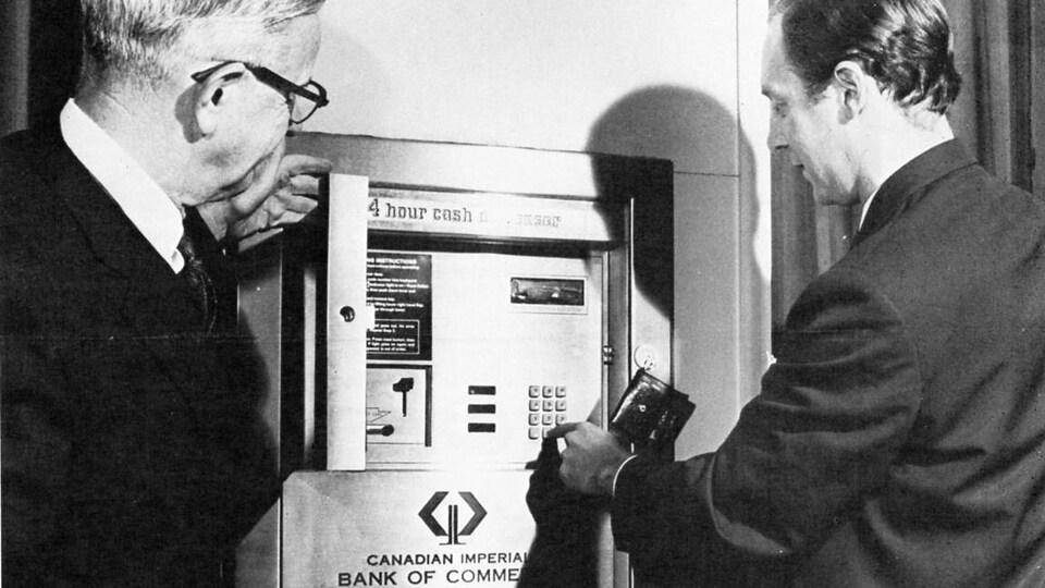 Deux hommes en train d’utiliser un des premiers guichets automatiques de la Banque CIBC.