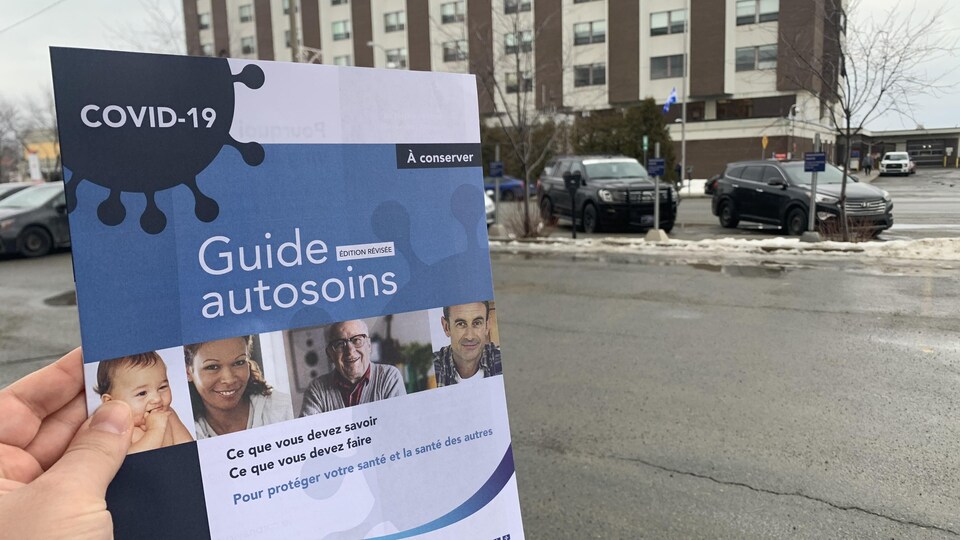Une femme tient le Guide autosoins reçu à la suite d'un test de dépistage de la COVID-19 près de l'hôpital de Rouyn-Noranda.