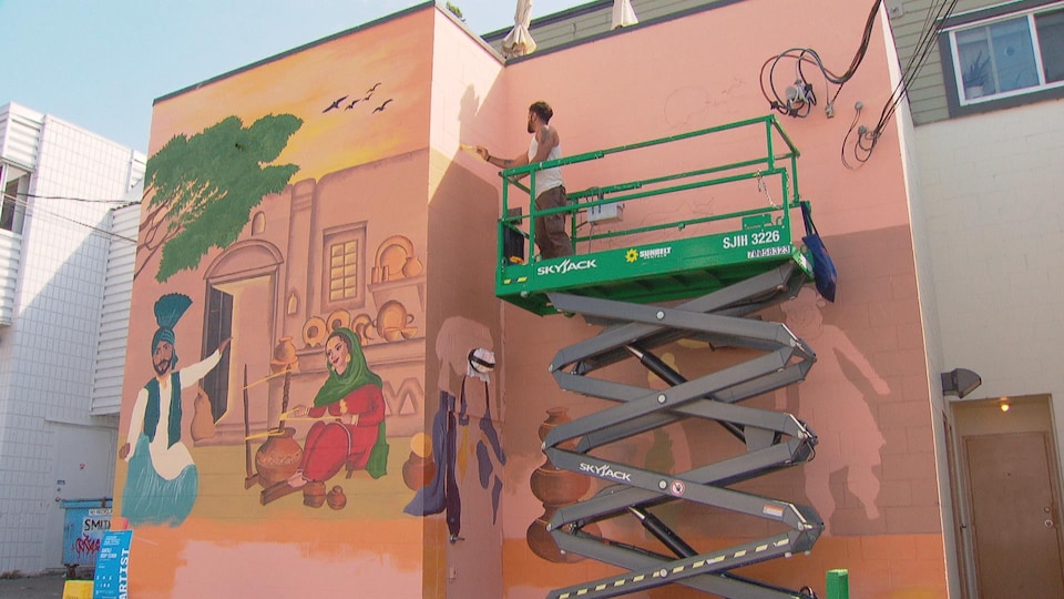 L'artiste Guntaj Deep Singh, debout sur un échafaudage, peint une murale.