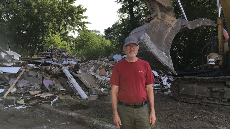 Un homme se tient devant un tas de ruines et une pelle mécanique. 