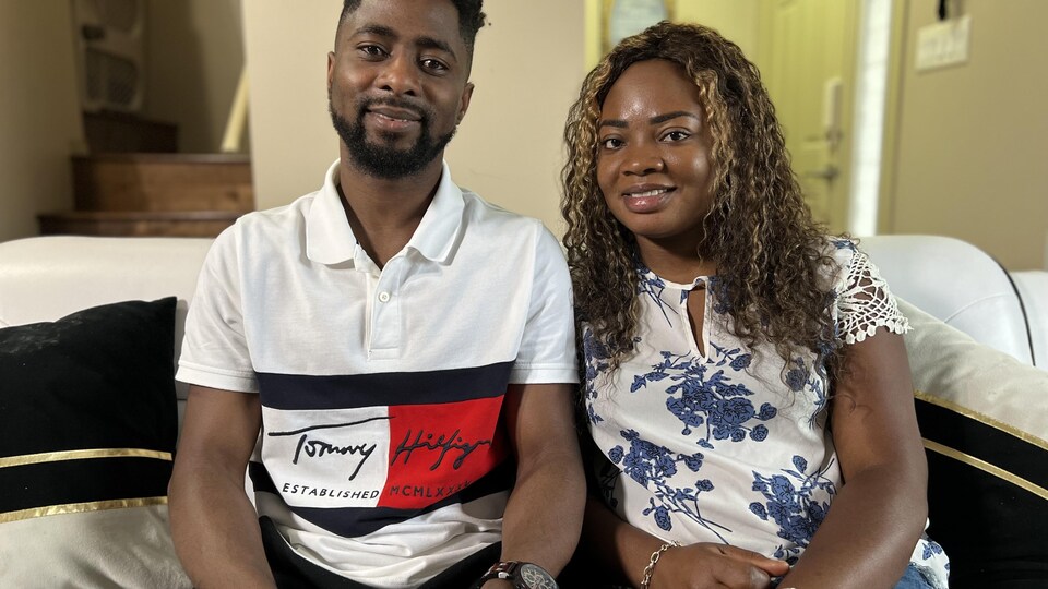 Un homme et une femme noirs sont assis sur leur canapé en souriant.