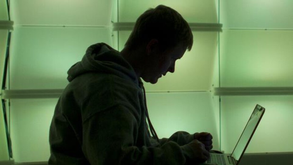 Une personne à contre-jour se sert d'un ordinateur portable dans un salon à  éclairage verdâtre aménagé pour le colloque des pirates informatiques Chaos Communication Congress, à Berlin.