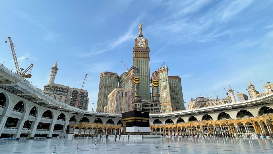 Quelques personnes se tiennent près de la Kaaba, une structure cubique, au centre de l'esplanade de la Grande mosquée de La Mecque.