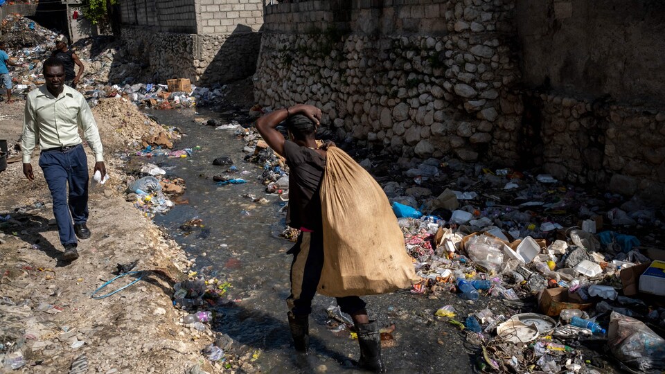 À Port-au-Prince, un homme qui porte un sac marche dans un ruisseau à travers les ordures.