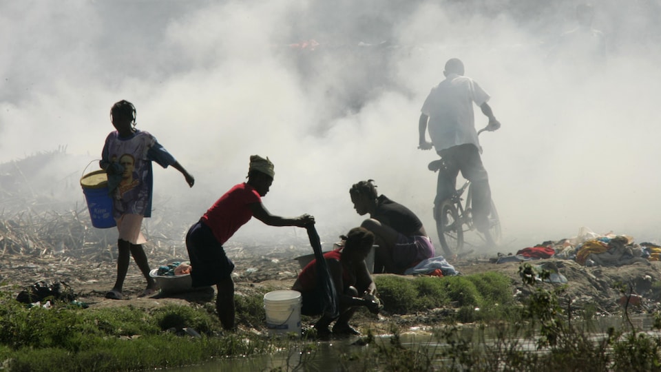 Des Haïtiennes lavent leur linge dans un ruisseau, alors que des ordures brûlent dans une décharge à L'Estère, le 18 janvier 2008