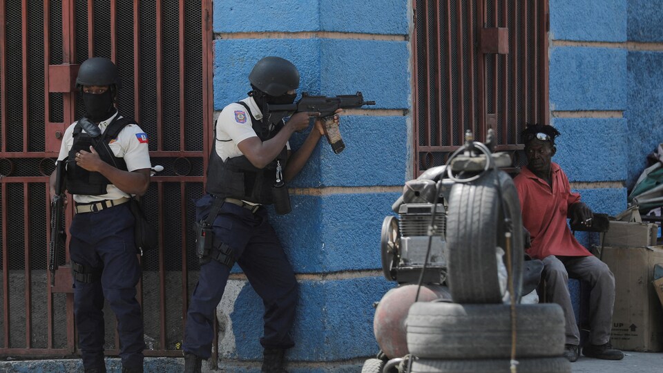 Two armed policemen stand on the corner of a building.