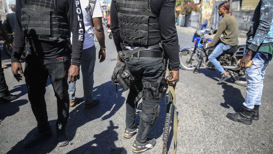 Des policiers armés dans une rue, entourés de manifestants.
