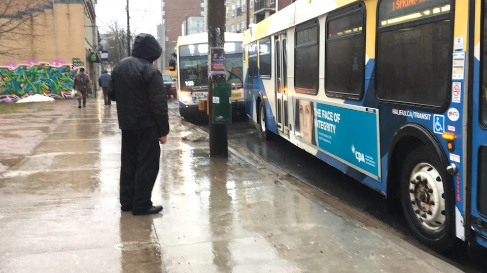 Un homme sous la pluie devant deux autobus qui s'arrêtent près du trottoir.