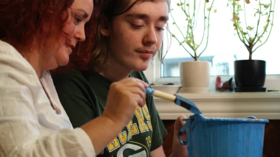 Une mère et son garçon peignent une citrouille en bleu.