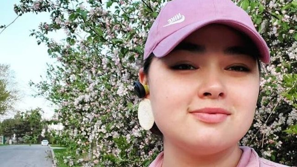 Hannah Tooktoo pose devant un arbre en fleur habillée d'un chemisier rose et d'une casquette rose.