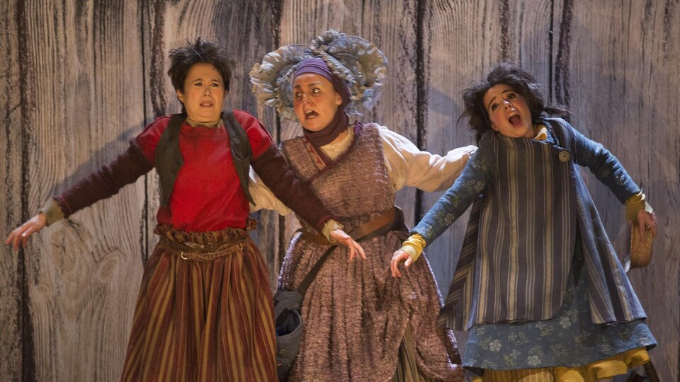 Trois personnes sont costumées sur scène. Une des trois tient les deux autres par le col de leurs vêtements et semble fâchée.
