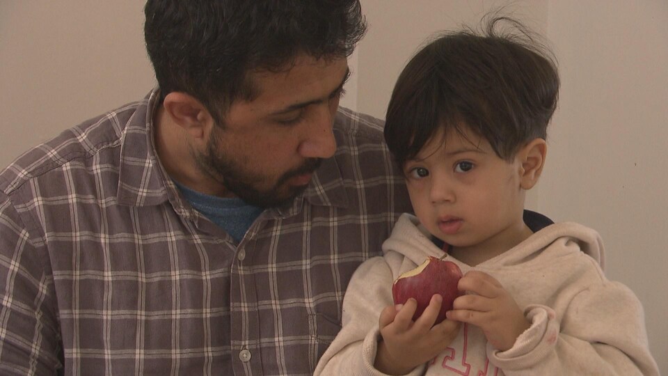 Un enfant est assis sur les genoux de son papa, mangeant une pomme.