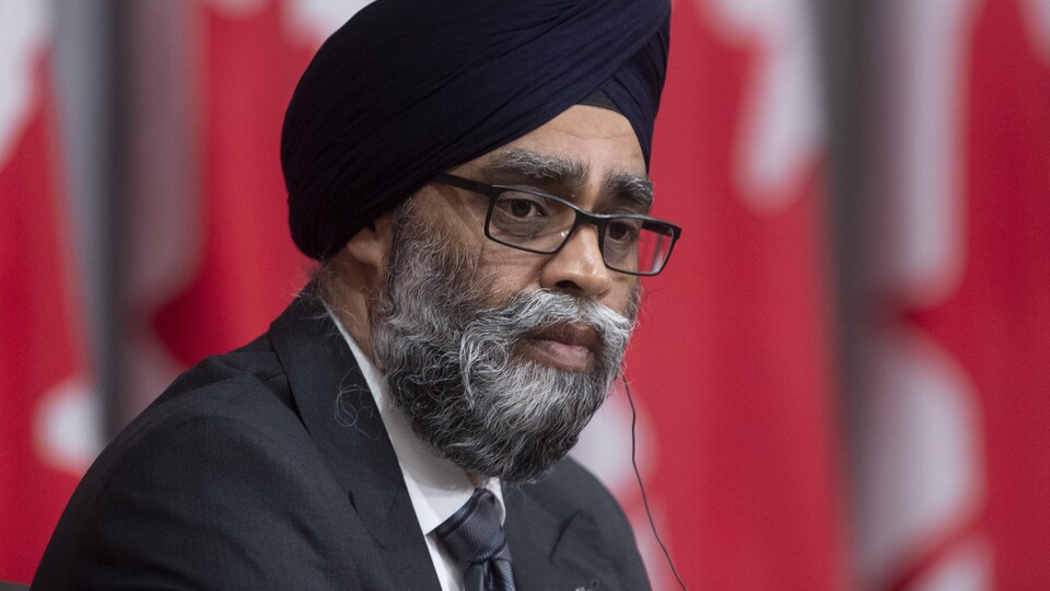 Harjit Sajjan devant une série de drapeaux canadiens.