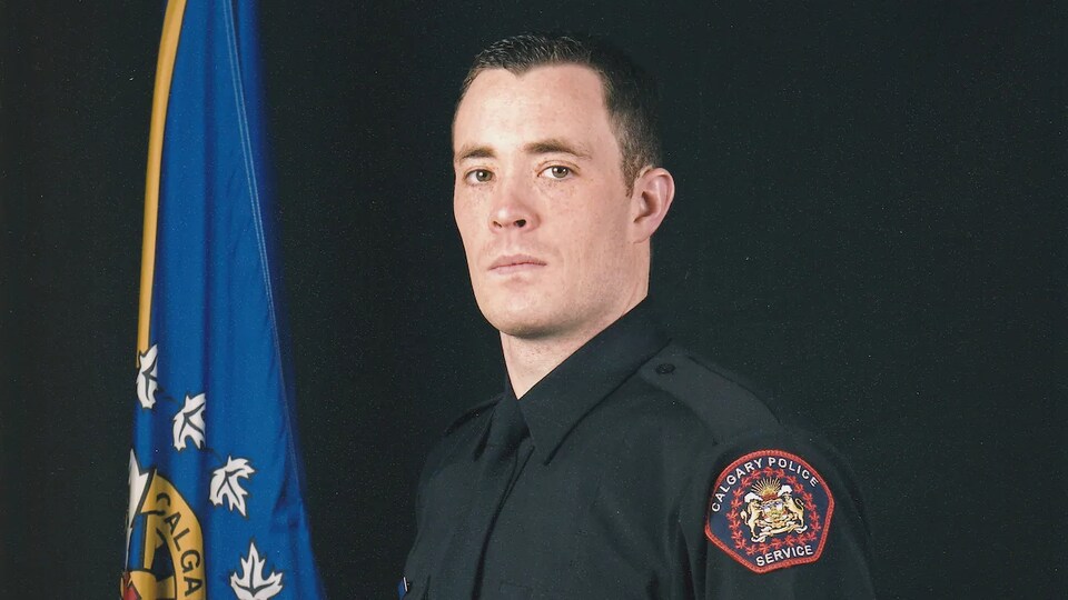 Le sergent Andrew Harnett, de la police de Calgar, pose debout en uniforme, sa casquette sous le bras droit.