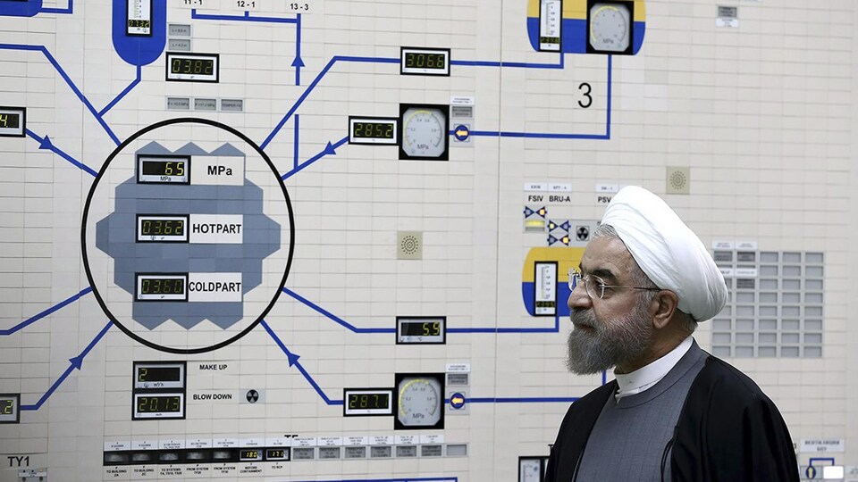 Le président iranien, portant la barbe mi-longue, des lunettes et un chapeau enturbanné, observe un mur où figure un diagramme et des cadrans analogiques.