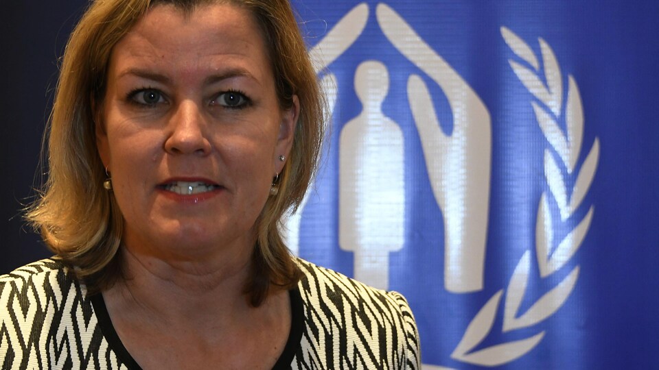 La vice-commissaire des Nations unies pour les réfugiés Kelly Clements devant un drapeau du Haut-Commissariat des Nations unies pour les réfugiés.