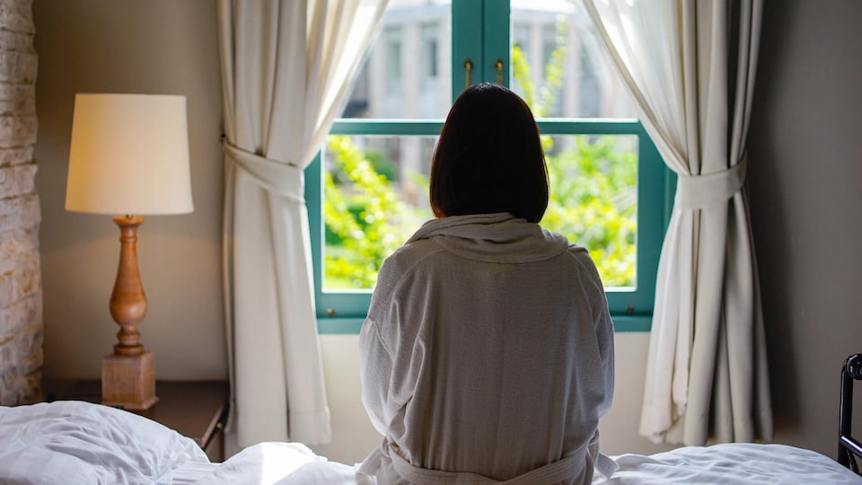 Une femme seule sur un lit, devant une fenêtre.