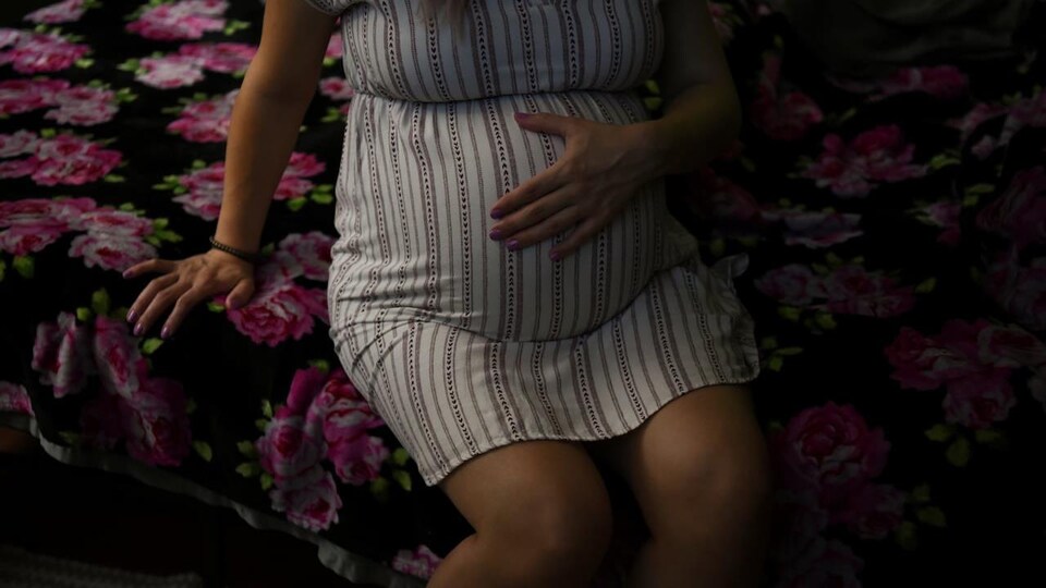 Une femme enceinte assise sur un lit tient son ventre.