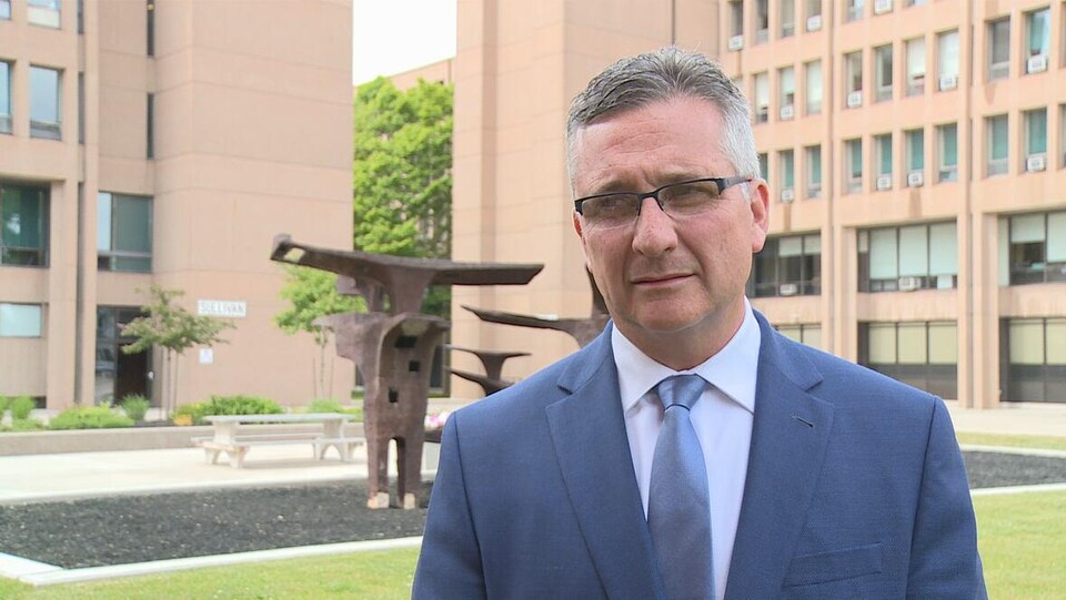 Un homme vêtu d'un complet bleu devant un bâtiment et une sculpture d'art public.