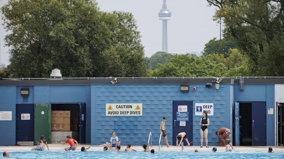 Des baigneurs dans une piscine avec la tour CN à l'horizon.