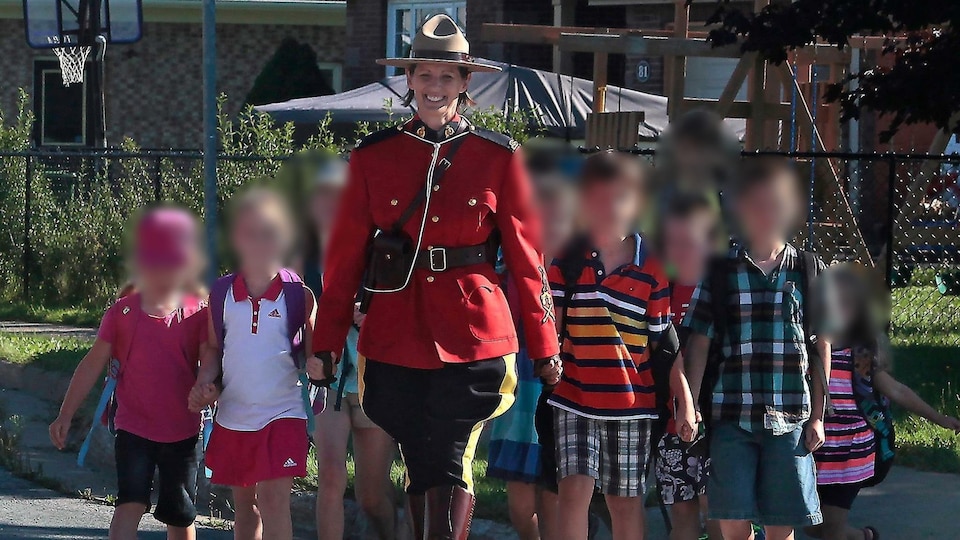 Heidi Stevenson porte l'uniforme de la Gendarmerie royale du Canada et marche avec plusieurs enfants dont les visages sont floutés.
