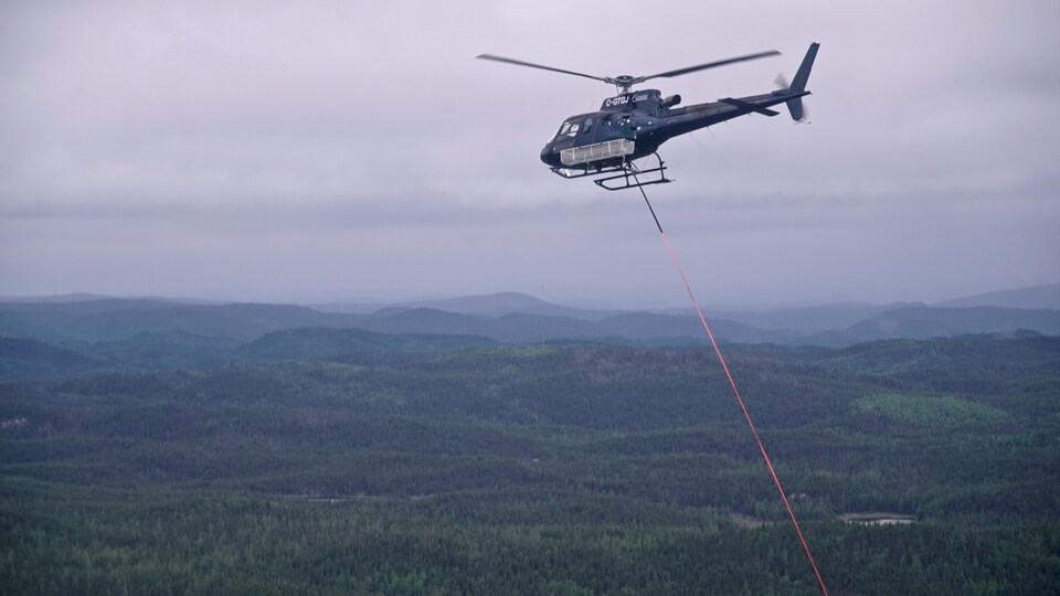 Un hélicoptère de la SOPFEU survole une forêt.