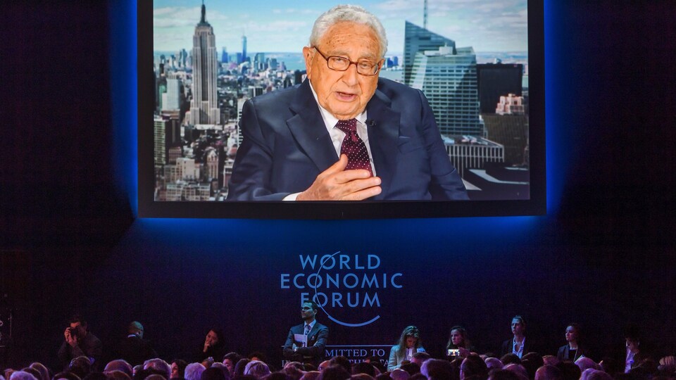 Henry Kissinger, sur un grand écran, s'adresse à des gens dans une salle lors du Forum économique mondial, en 2017.