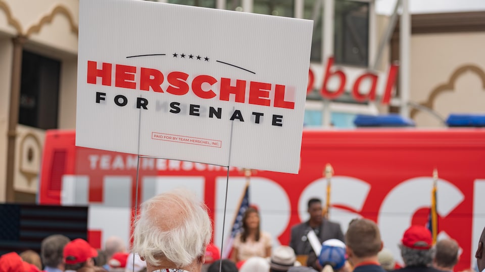 Des gens sont réunis dans un rassemblement partisan. Sur l'une des pancartes, on peut lire « Herschel for Senate ».