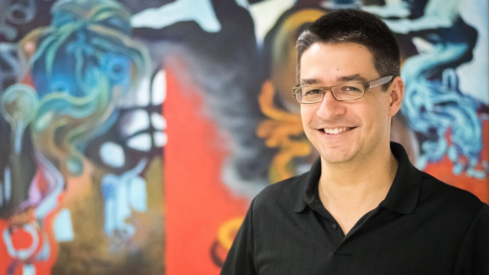 Une photo de Pierre-Alexandre Fournier, souriant, devant une toile très colorée.