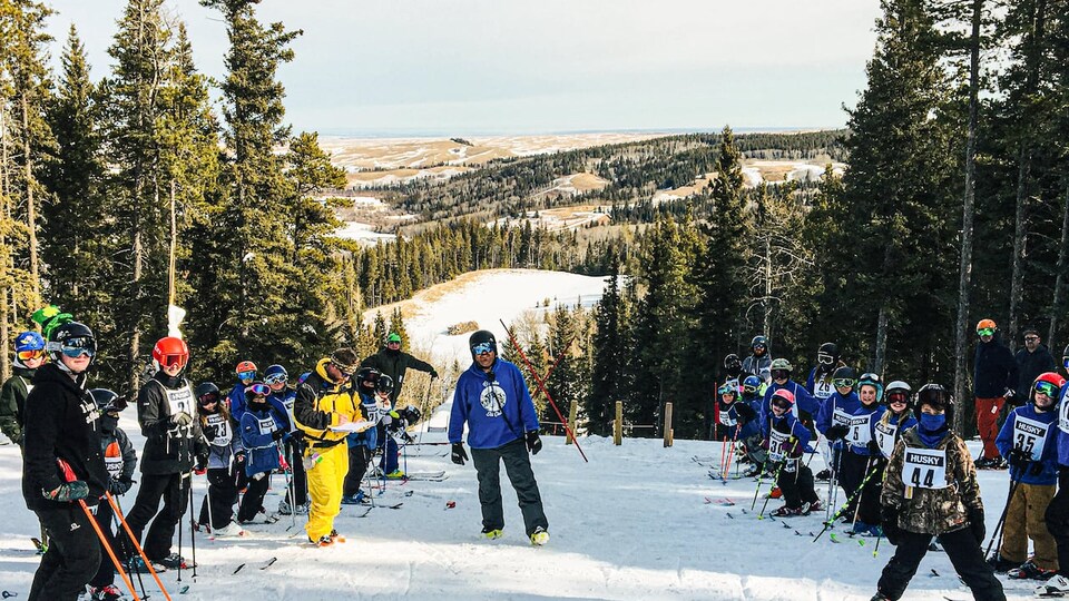Des dizaines de skieurs sont alignés le long d'une piste avec une montagne en arrière-plan.
