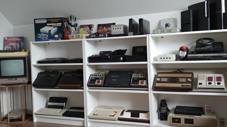 Des étagères où sont placées des dizaines de consoles de jeu vidéo de toutes les époques.