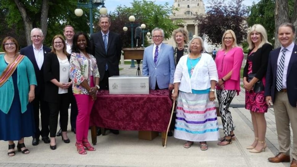 Le premier ministre ainsi que quelques membres du gouvernement et des leaders communautaires debout devant le palais législatif du Manitoba.