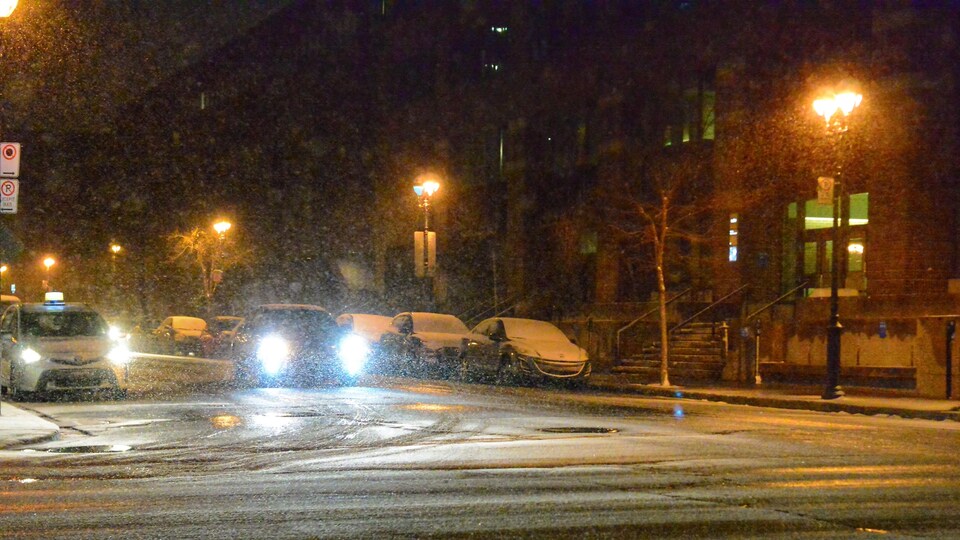 Une voiture roule dans la noirceur tandis que la visibilité est réduite par de la neige qui tombe.