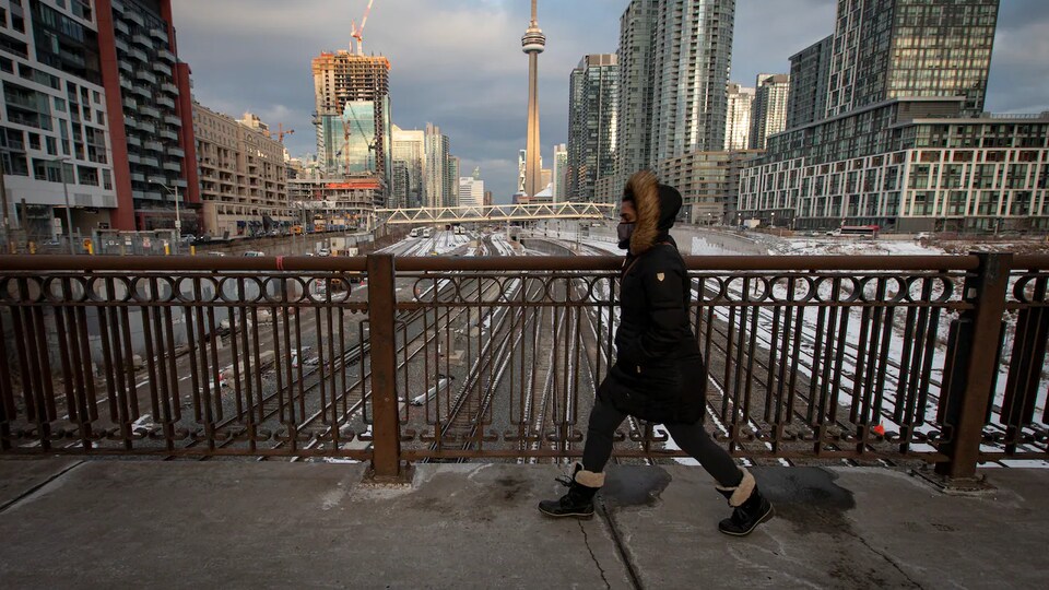 Une femme marche sur un viaduc au-dessus d'un couloir ferroviaire à Toronto.