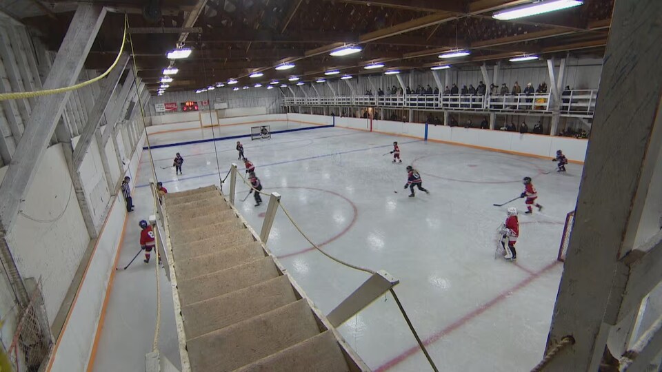 Des jeunes joueurs de hockey sur une patinoire surplombée par une passerelle.