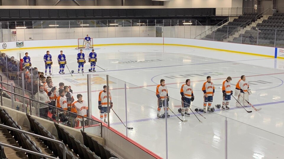 Des joueurs alignés avant le match sur la glace, les gradins sont vides.