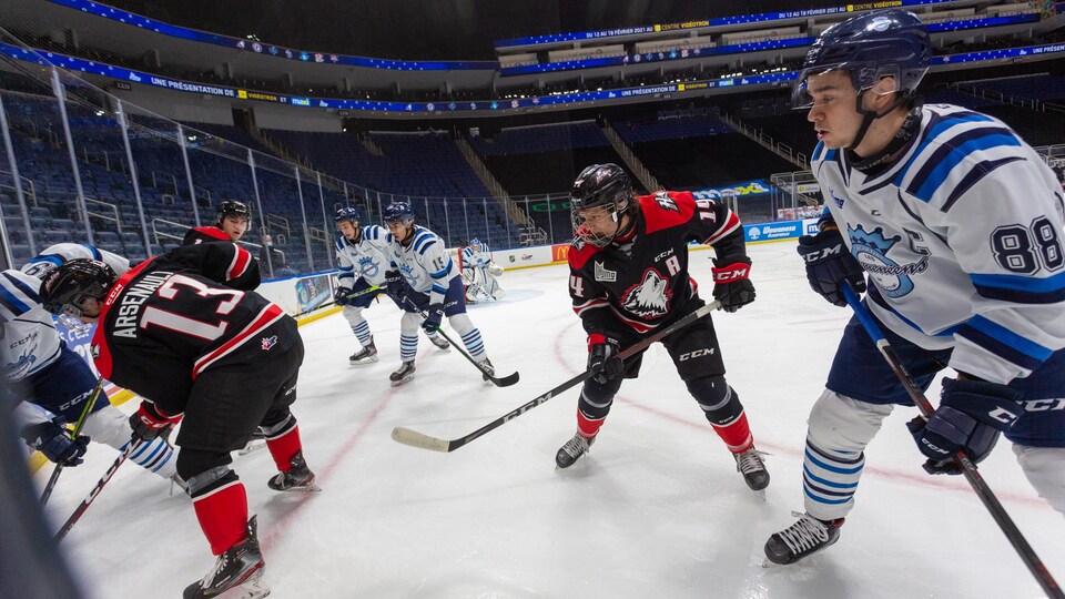Des joueurs de hockey bataillent pour la rondelle dans une aréna vide.