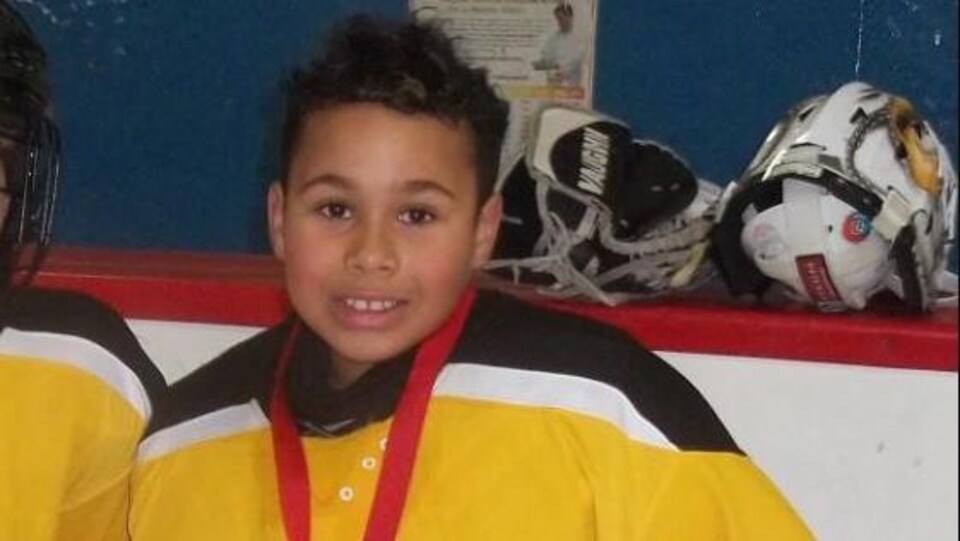 Un garçon vêtu d'un équipement de gardien de but pose avec une médaille au cou. 