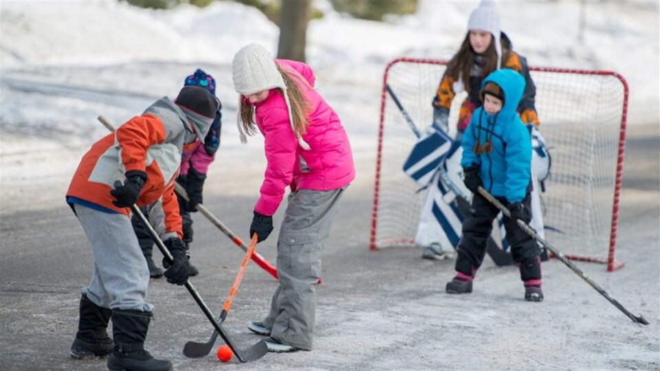 Des enfants jouent au hockey dans la rue, en hiver.