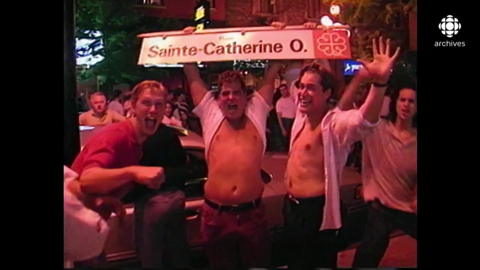 Trois hommes agités tiennent un panneau de signalisation routière de la rue Sainte-Catherine Ouest à Montréal.