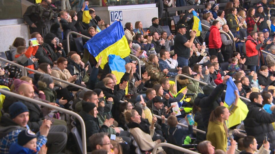 Des spectateurs applaudissent, sont souriants ou montrent leurs drapeaux aux couleurs de l'Ukraine lors de la partie des Bisons du Manitoba et de l'équipe nationale ukrainienne, le 9 janvier 2023 au centre Canada Life à Winnipeg.