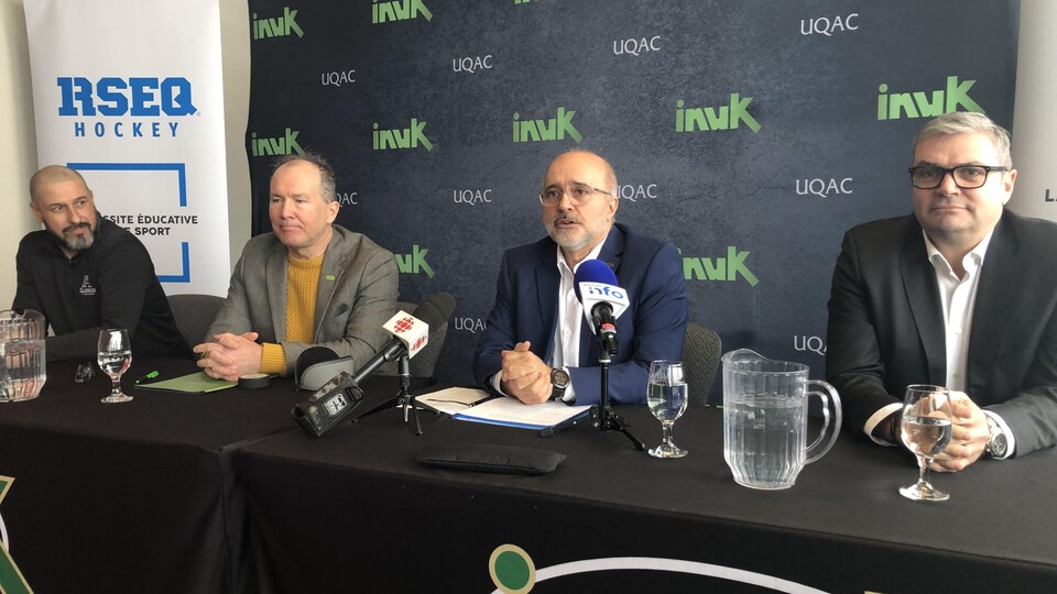 Quatre hommes assis derrière une table en conférence de presse.