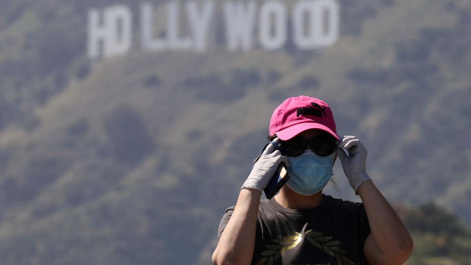 Une personne portant un masque et des gants avec l'écriteau Hollywood en arrière plan