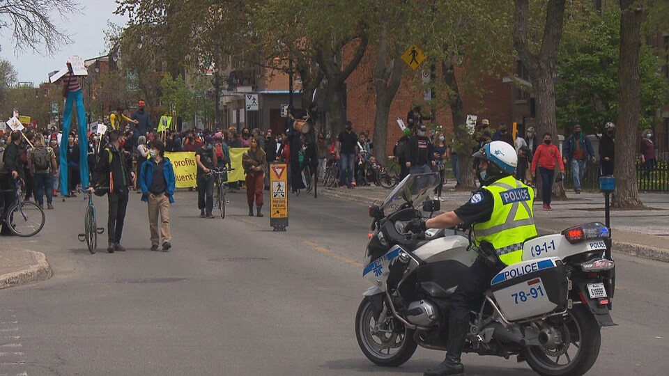 Des citoyens défilent dans la rue avec un policier à moto devant.