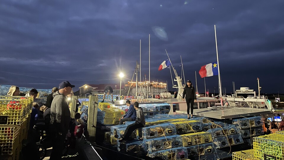 Plusieurs personnes sur le quai à l'aube devant les bateaux de pêche chargés de casiers à homard.